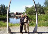 Alaska Trip - Anchorage - Alaska Native Heritage Center - Bowhead Whale Jaw Bones - Just outside the Inupiaq St Lawrence Island Yupik Village exhibits are two jaw bones from a bowhead whale embedded in the ground forming an arch. Lucinda and Ed found an obliging fellow tourist who took this picture of them framed by the arch. Lake Tiulana and the Center's main building is in the background. Alaska Trip - Anchorage - Alaska Native Heritage Center - Bowhead Whale Jaw Bones